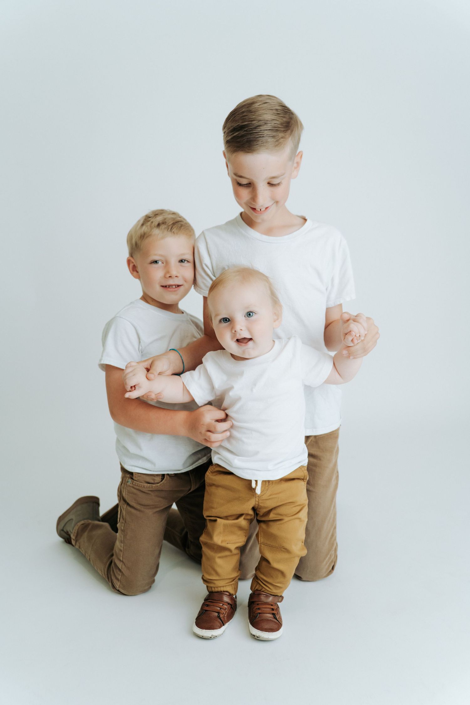 Three blonde brothers in white shirts pose together for a studio family portrait.
