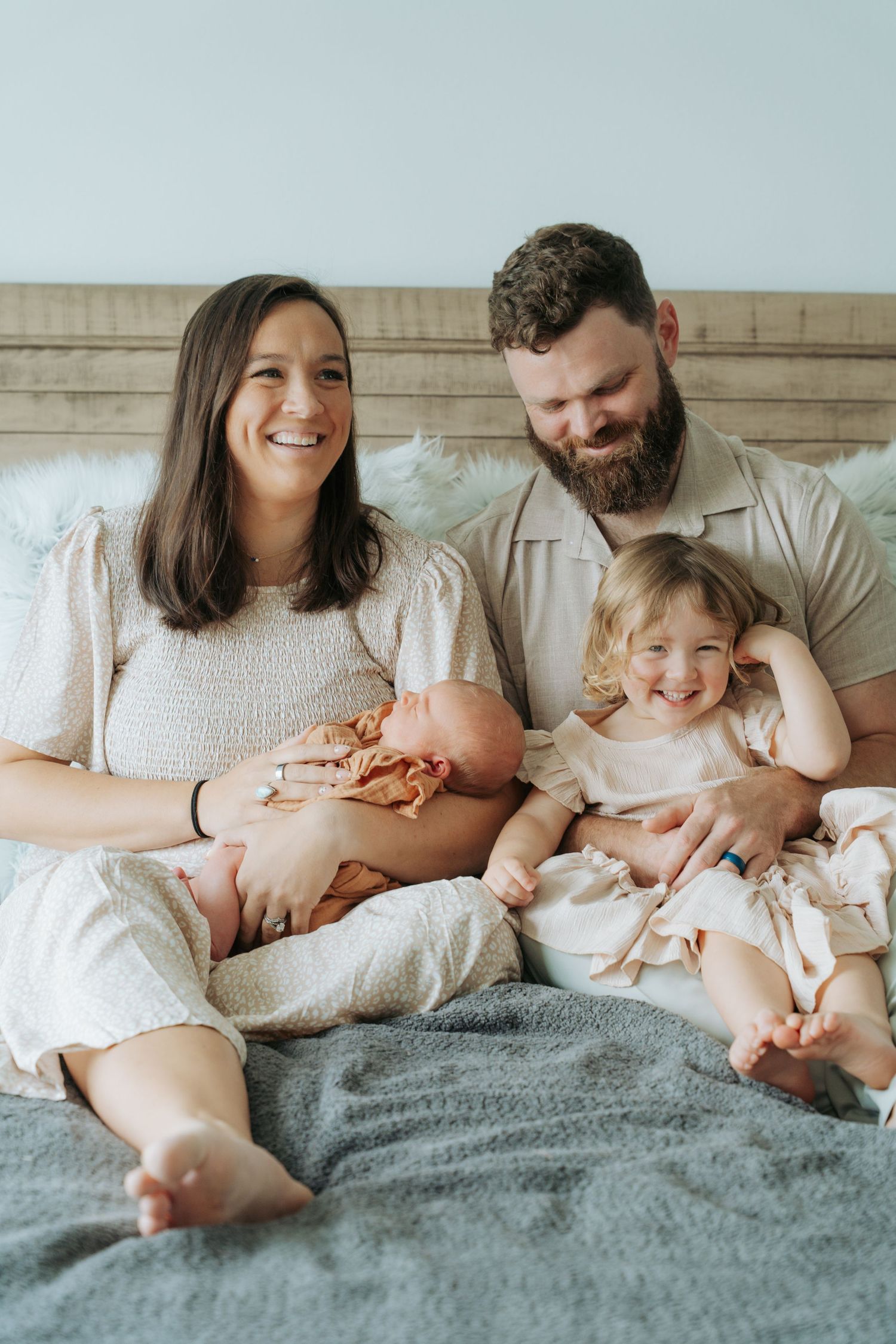 Joyful family portrait of parents and two children sitting together on a gray bed at home.