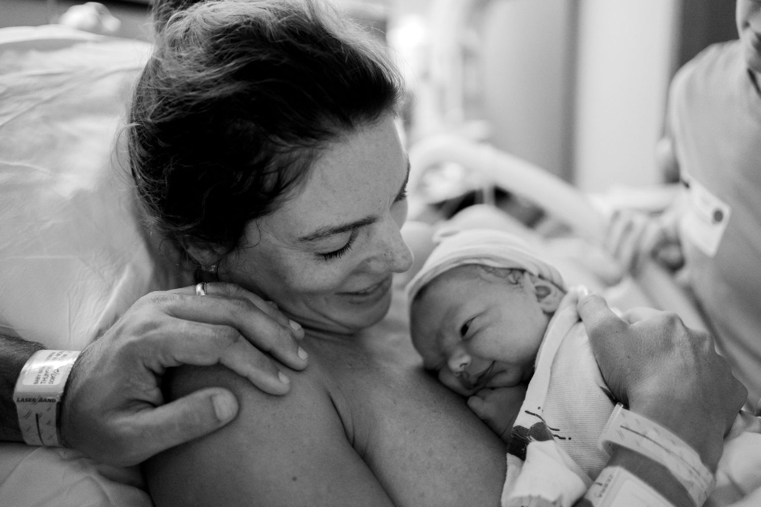 Black and white photo of a mother smiling at her newborn baby in a hospital room after birth.