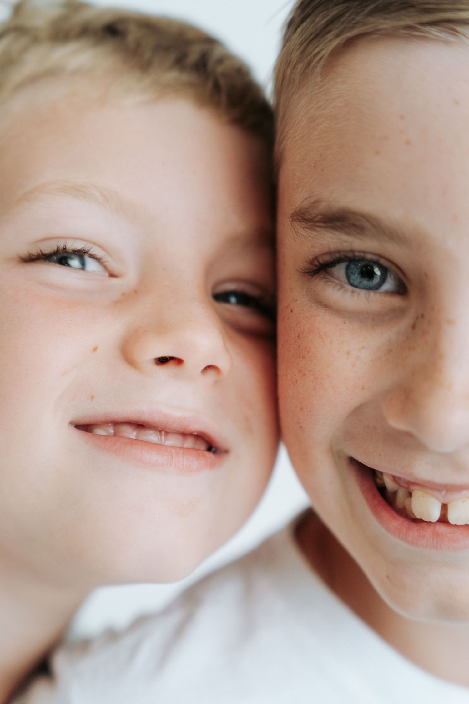 Close-up portrait of two smiling freckled brothers with blue eyes and light hair pressed together.