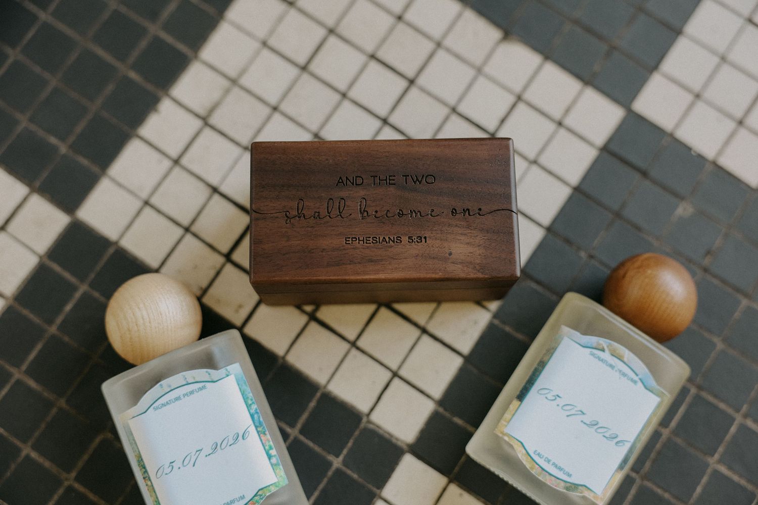 Wooden keepsake box with engraved text beside two glass perfume bottles on tiled surface.