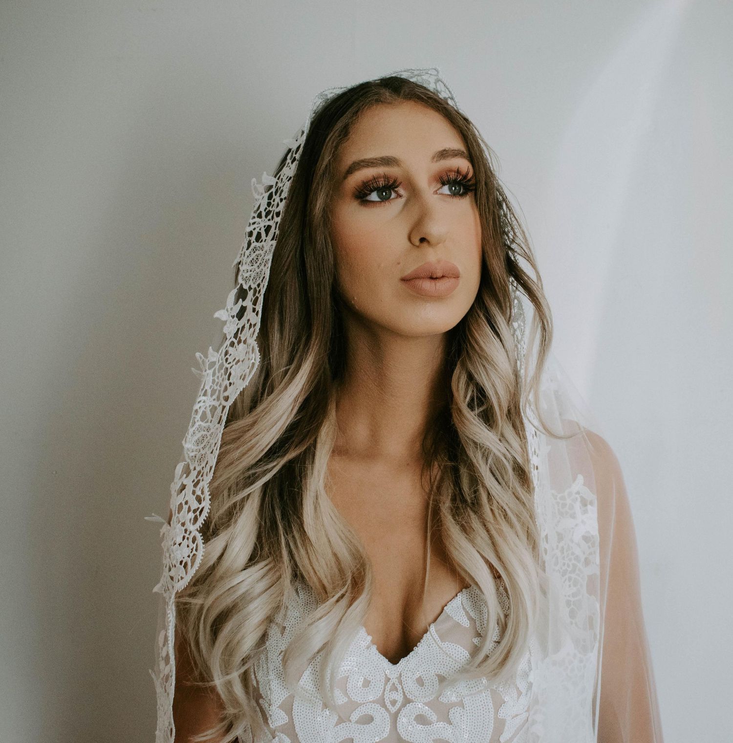 Bride wearing lace wedding dress and veil with glamorous makeup and long wavy ombre hair.