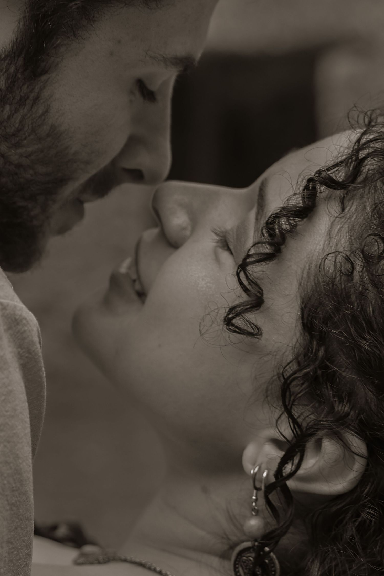 Intimate black and white close-up portrait of couple about to kiss with curly-haired woman smiling.
