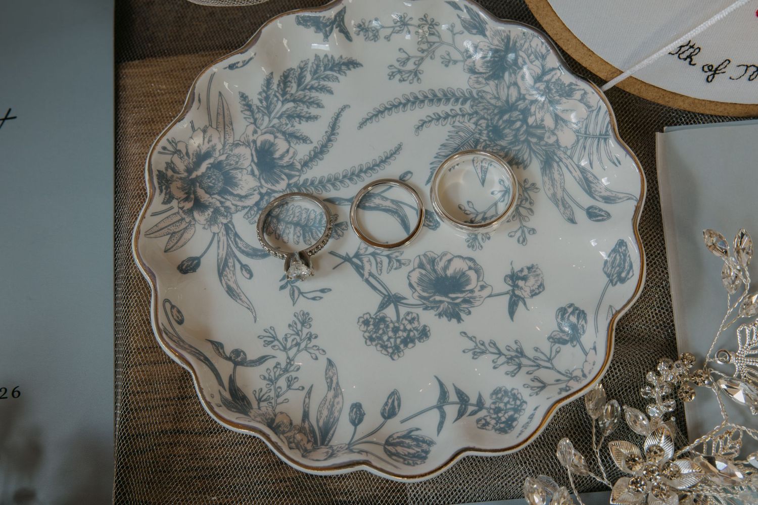 Blue and white floral porcelain ring dish holding two gold wedding bands on a rustic wooden surface.