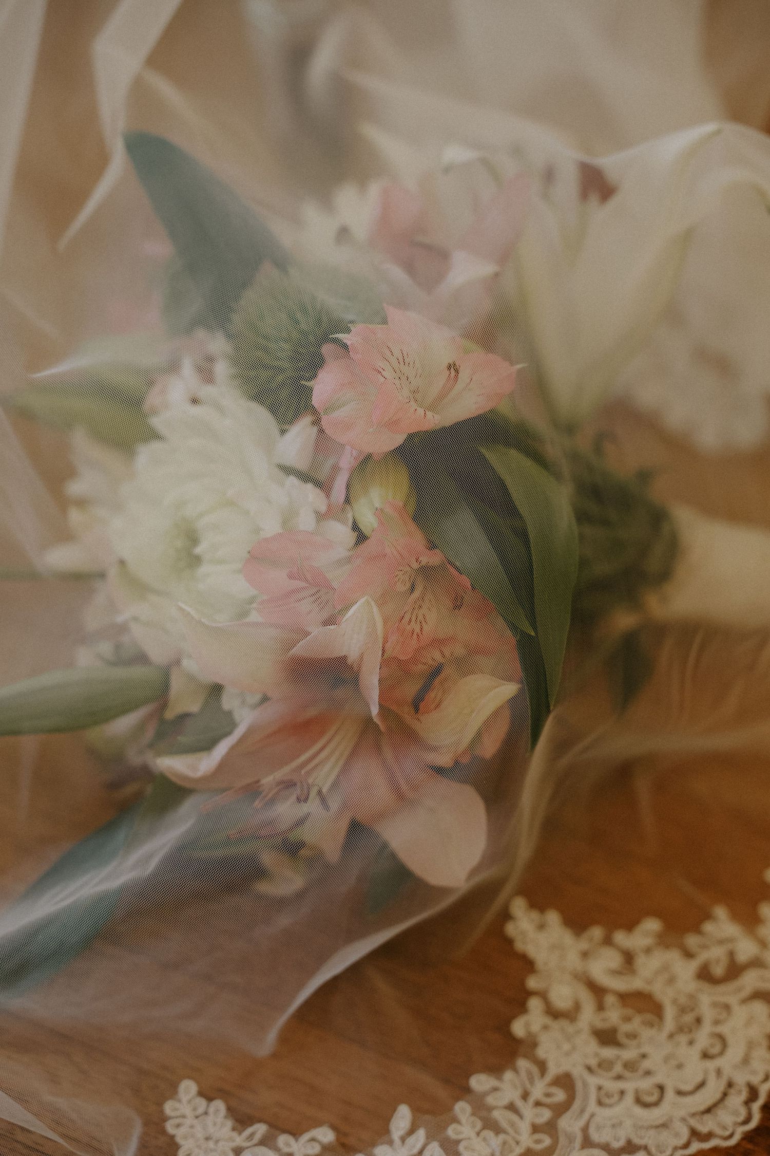 Soft romantic bridal bouquet with pink alstroemeria and white flowers under delicate tulle veil.