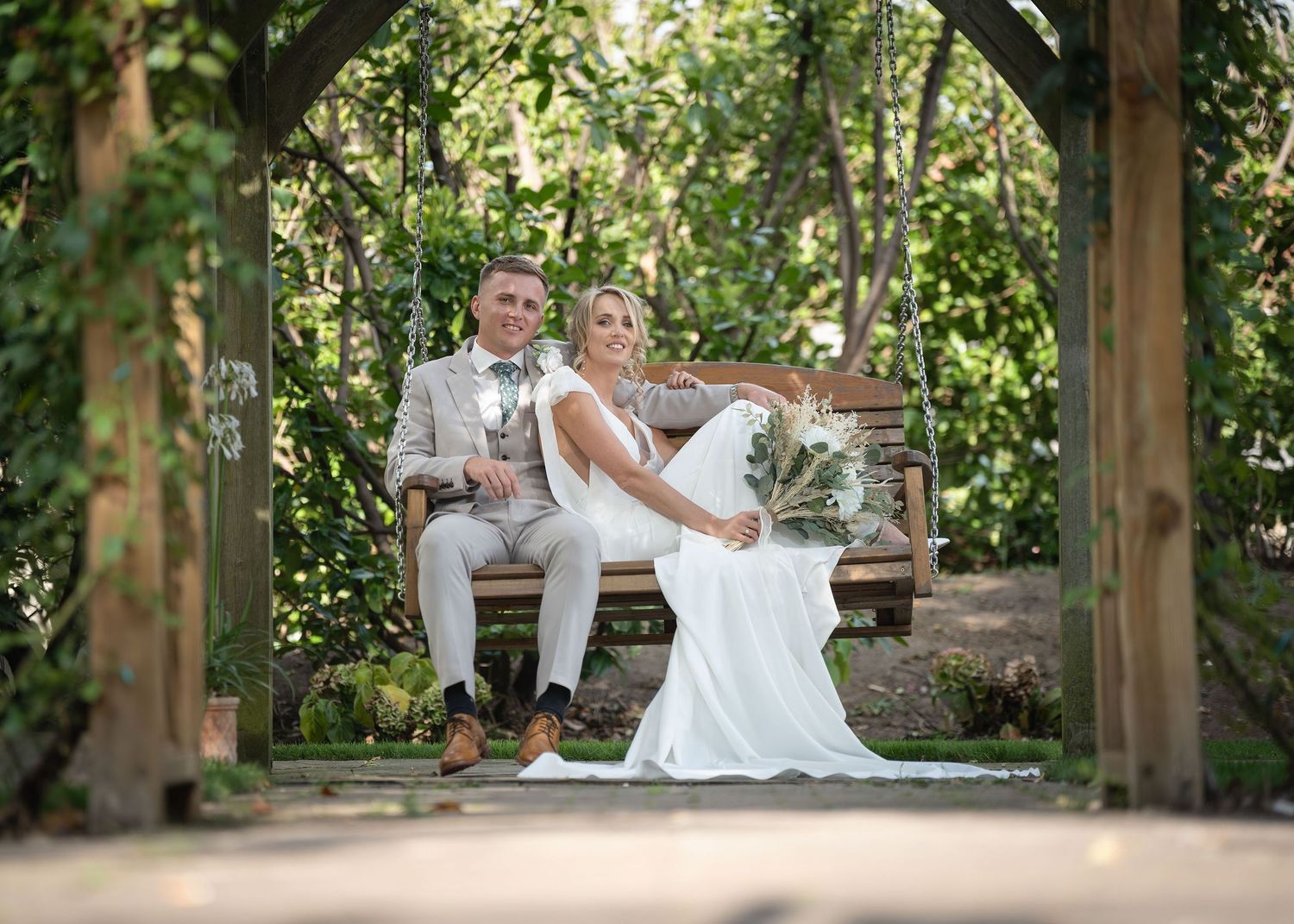 Bride and groom sitting together on a bench while posing for the camera.