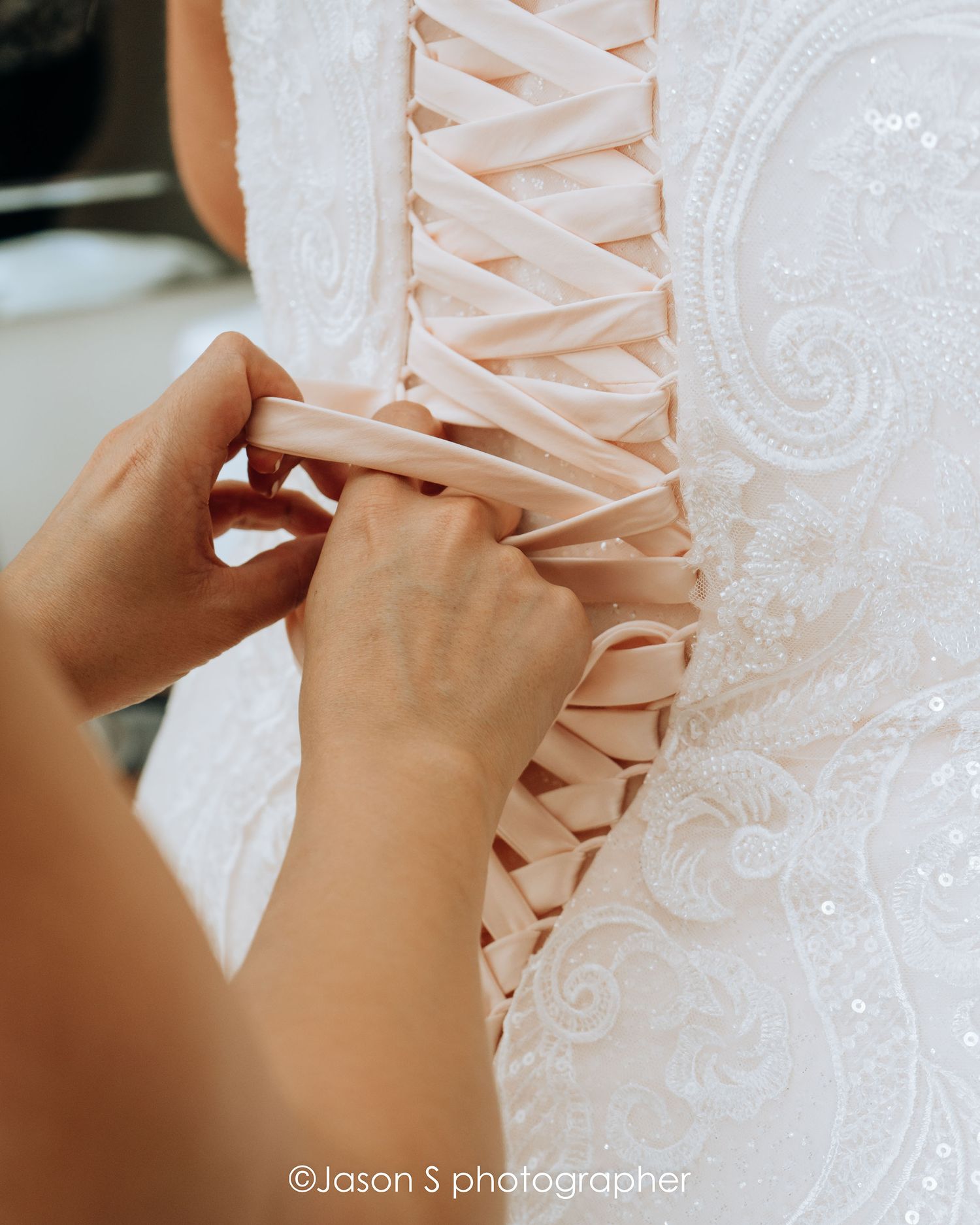 Bridesmaid fastening the bride’s corset before the ceremony.