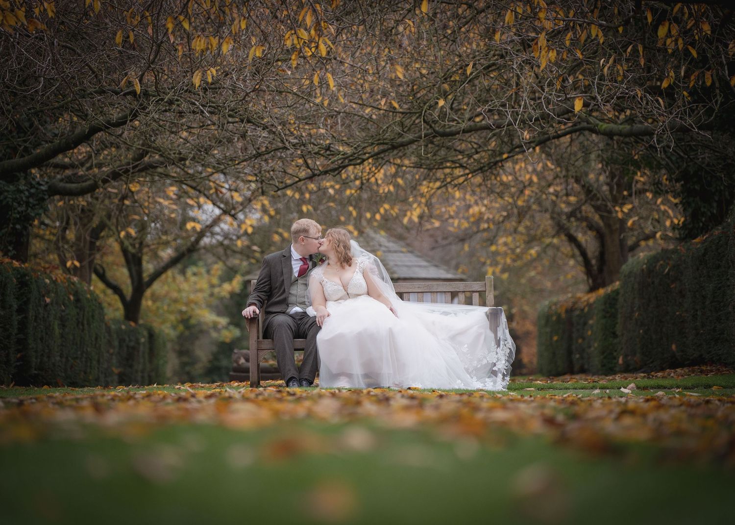 Bride and groom sitting together on a bench while posing for the camera.