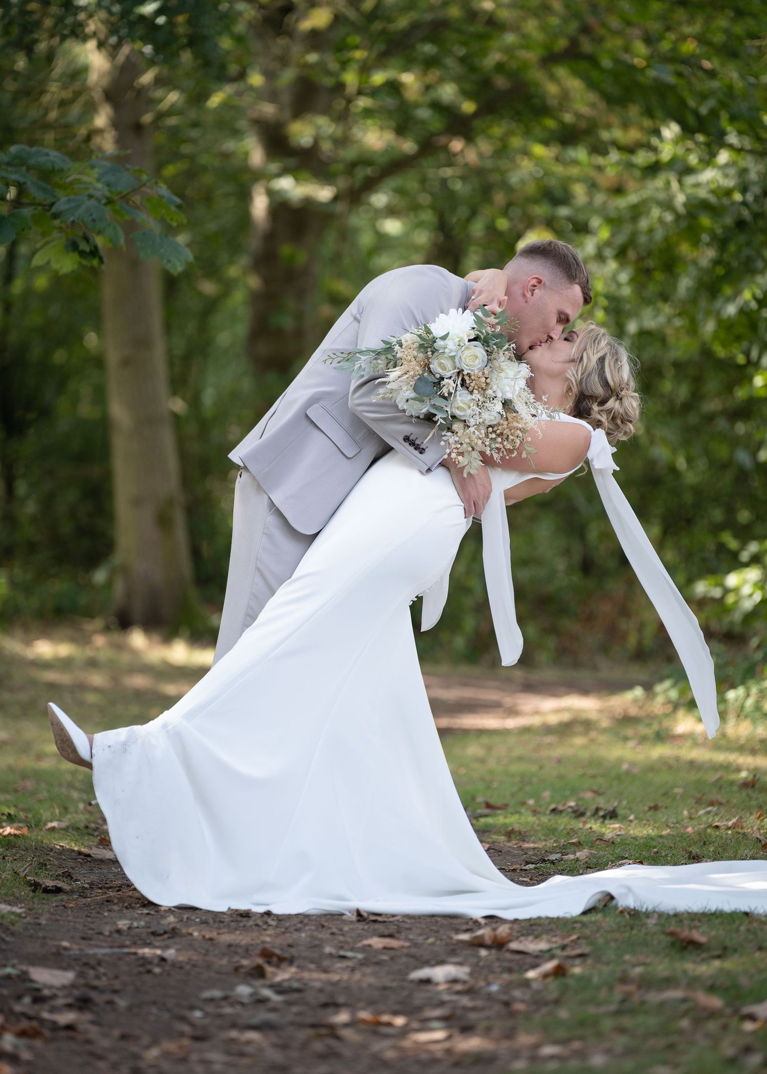 The bride and groom sharing a kiss while standing together in a forest.