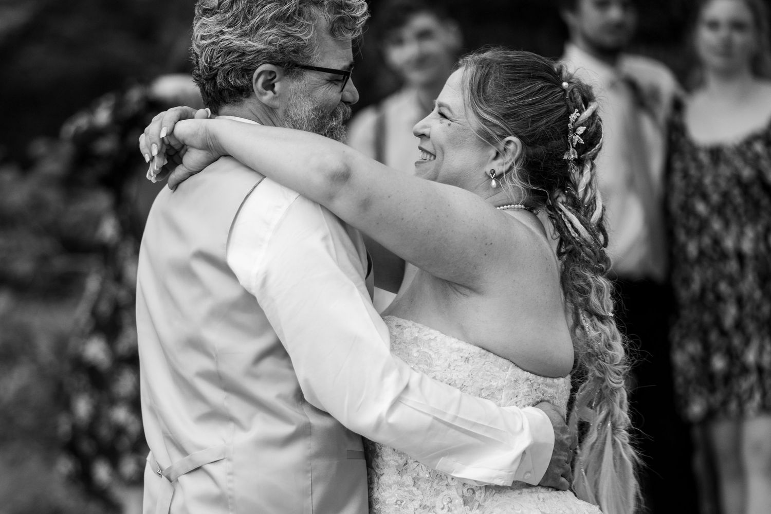 Black and white close-up of smiling bride embracing groom during romantic first dance at wedding.