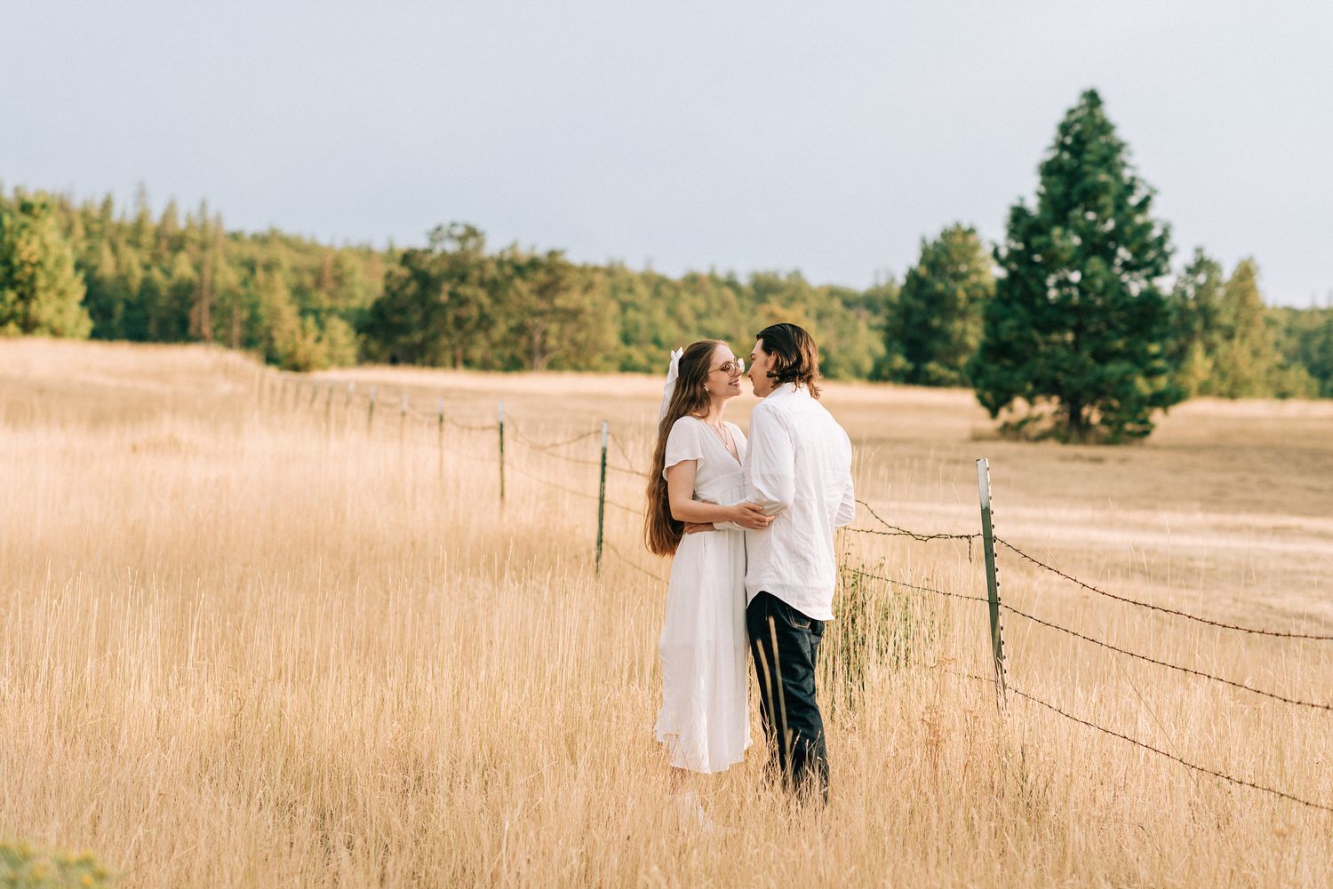 Couple strolls through a rustic field with wooden fence posts.