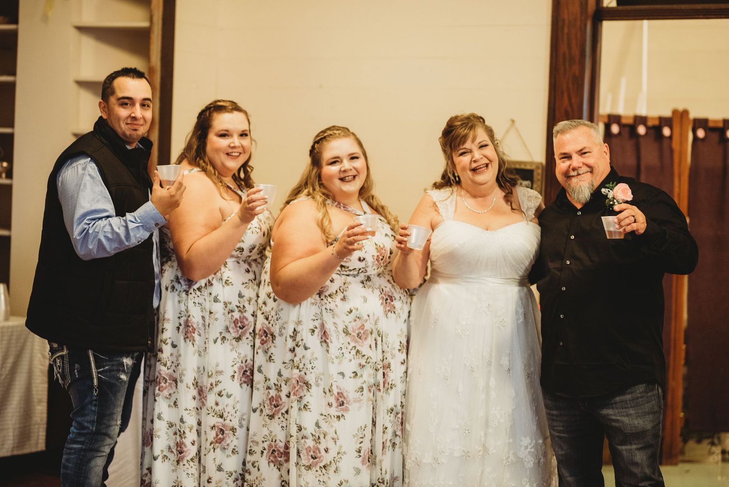 A group celebrates at a rustic indoor wedding reception with wooden beams and warm lighting.