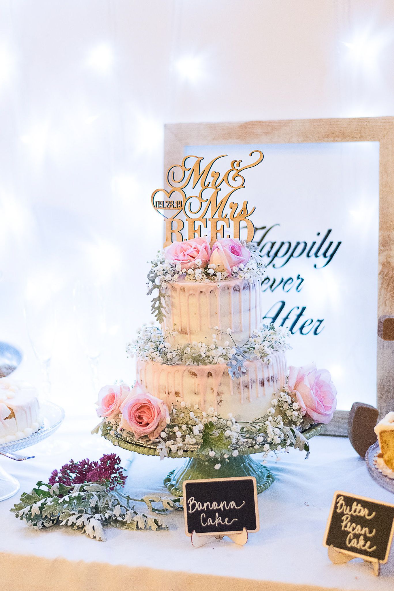Wedding cake display with dessert menu signs and floral decorations.