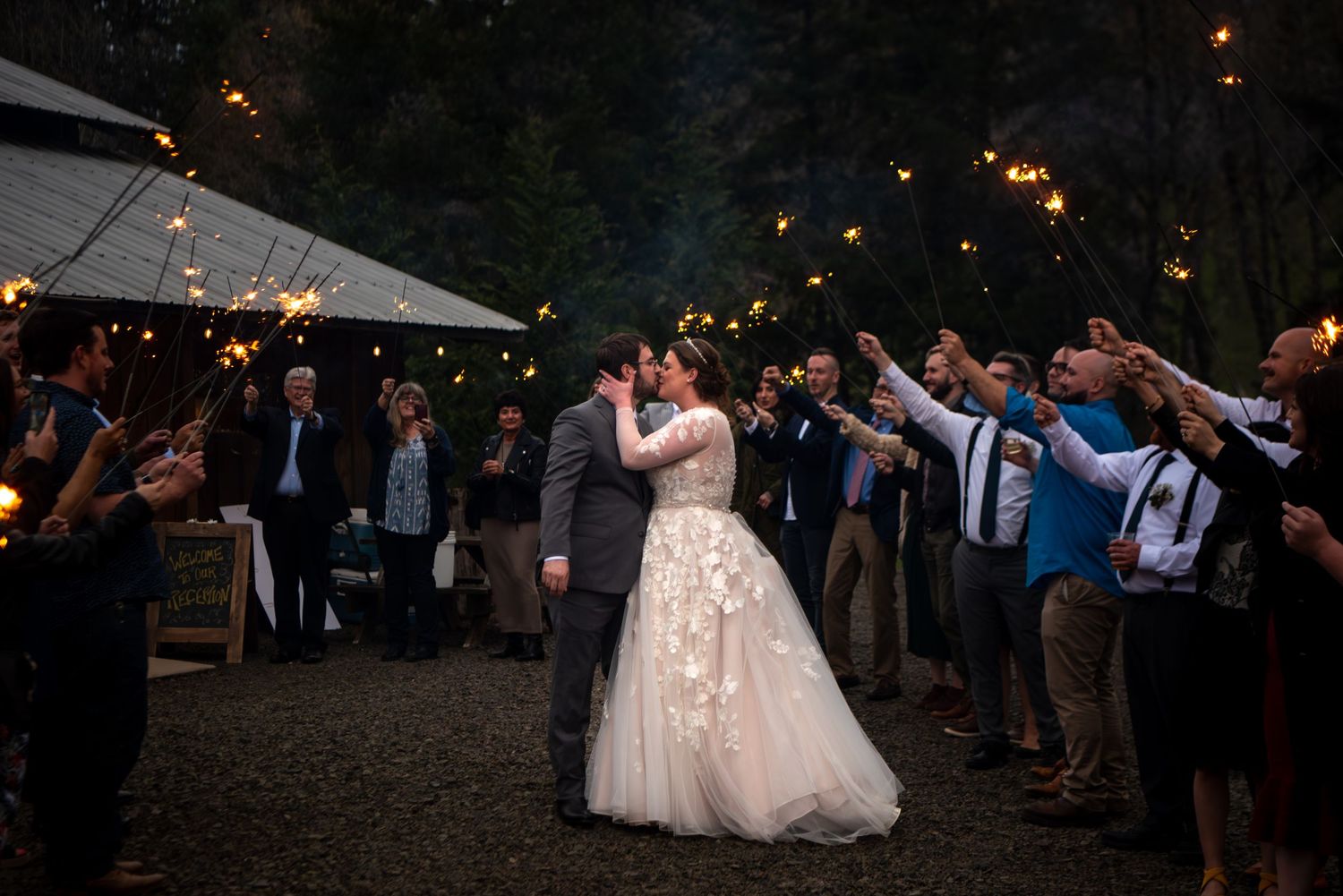 Bride and groom sharing a magical kiss surrounded by guests holding sparklers at their outdoor evening wedding.