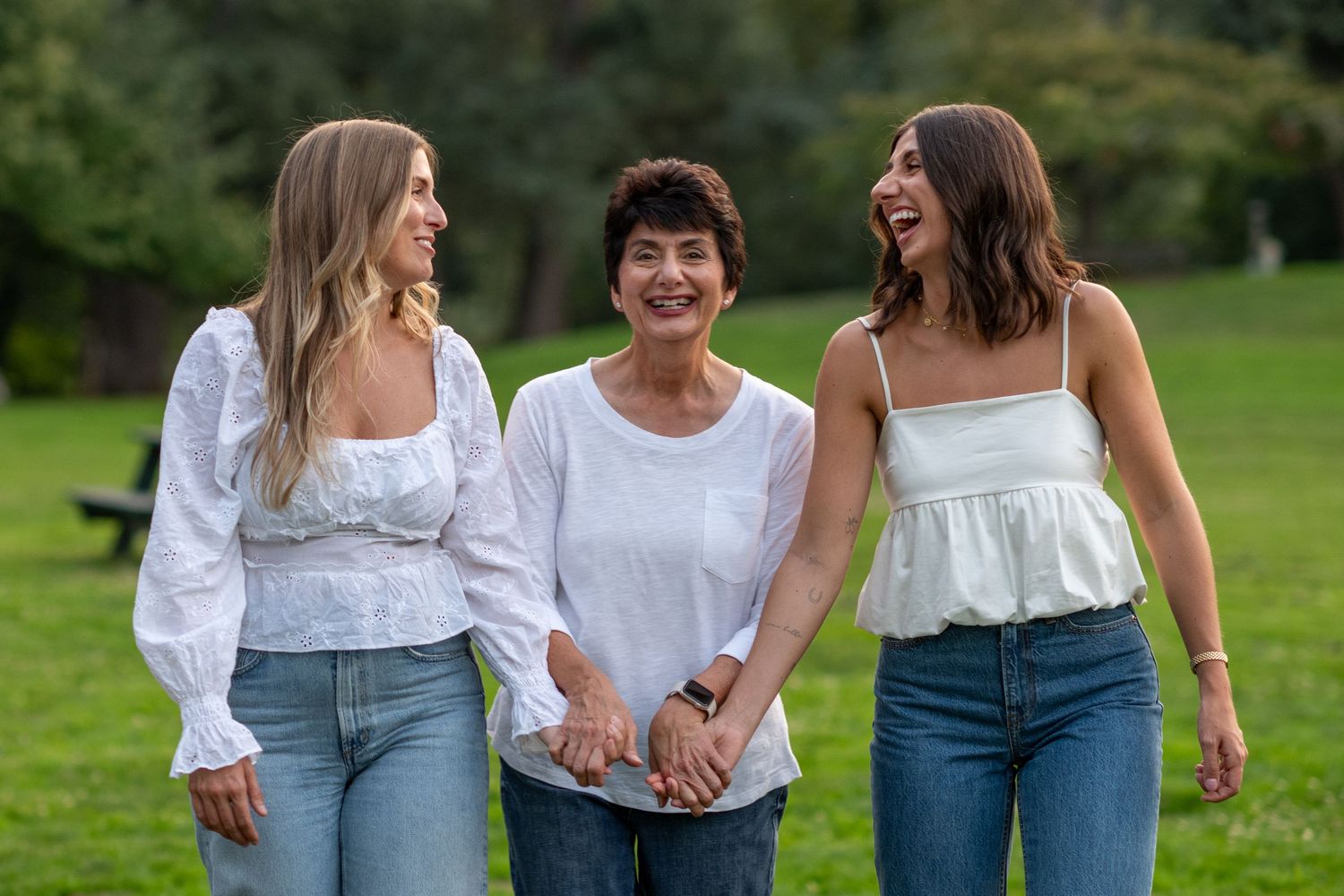 Mother and two daughters laughing and holding hands while walking on a green lawn.