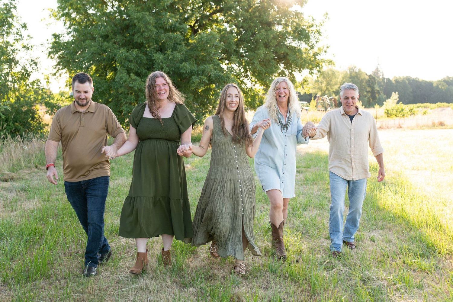 Happy family of five holding hands and walking together through a sunny green field during outdoor portrait session.