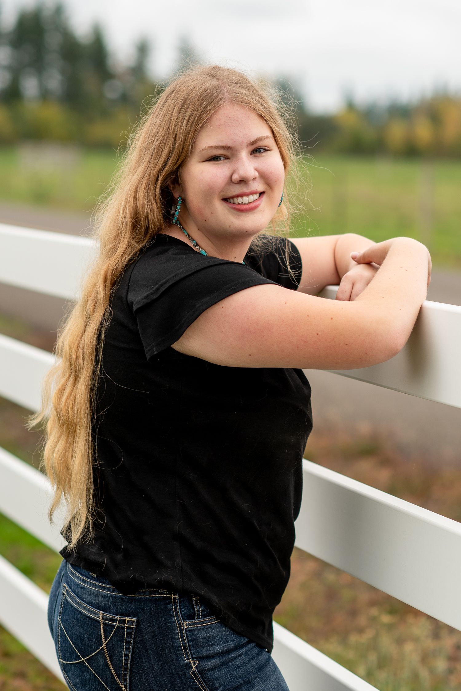 A person in casual attire leans against a white fence on a rural farm.