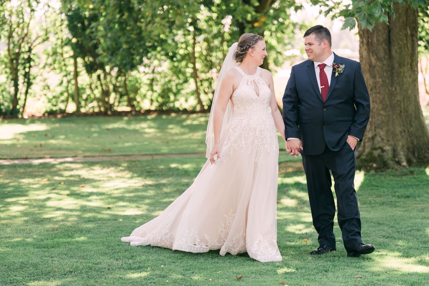 Wedding party poses on a lush green lawn under mature trees on a sunny day.