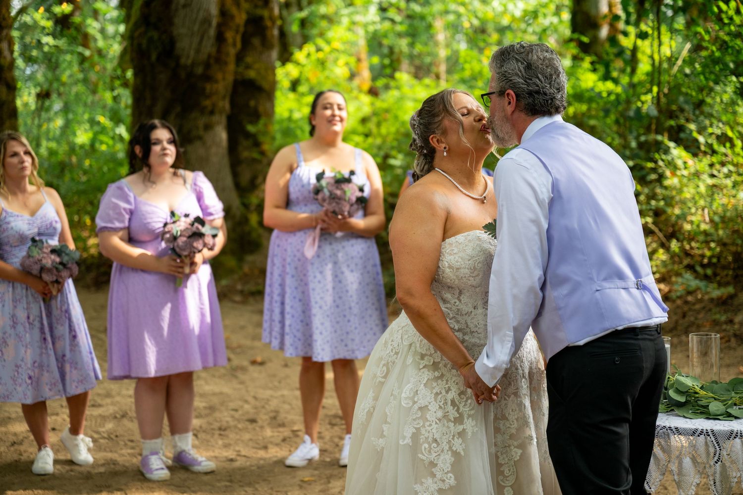 Wedding ceremony moment in a forest setting with bridesmaids in purple dresses.