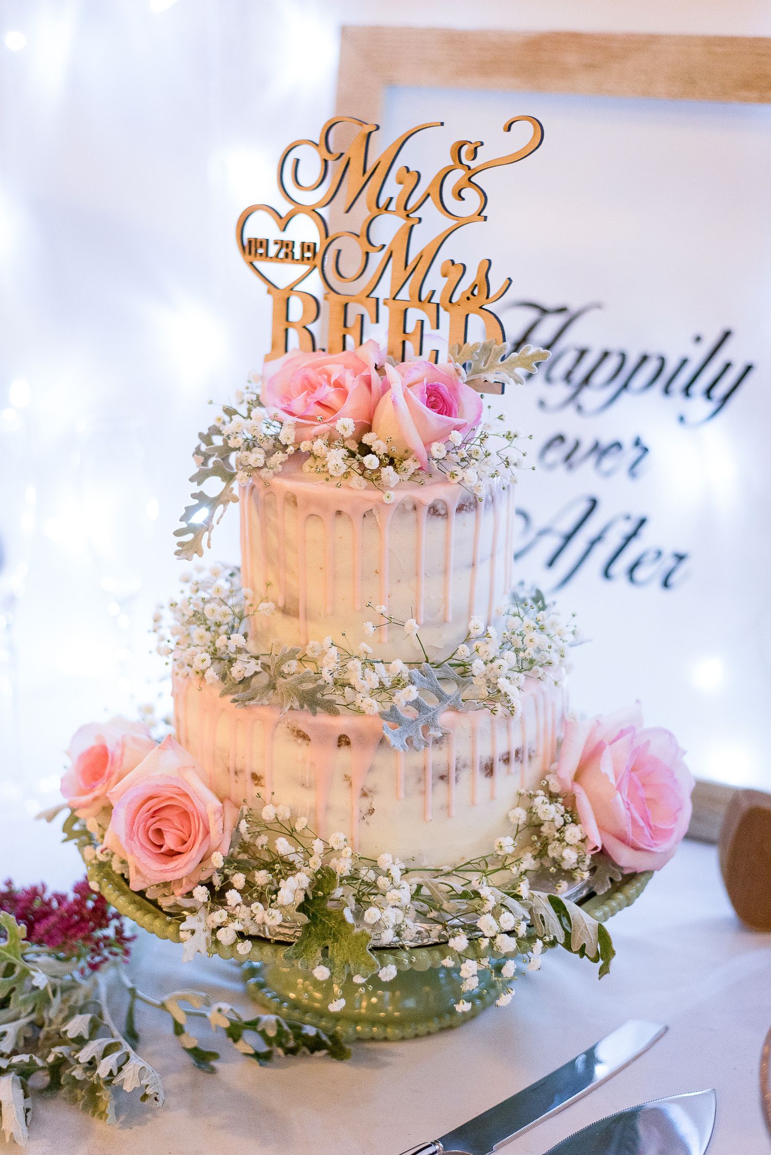 Elegant white wedding cake decorated with pink roses and baby's breath with a Mr & Mrs topper.