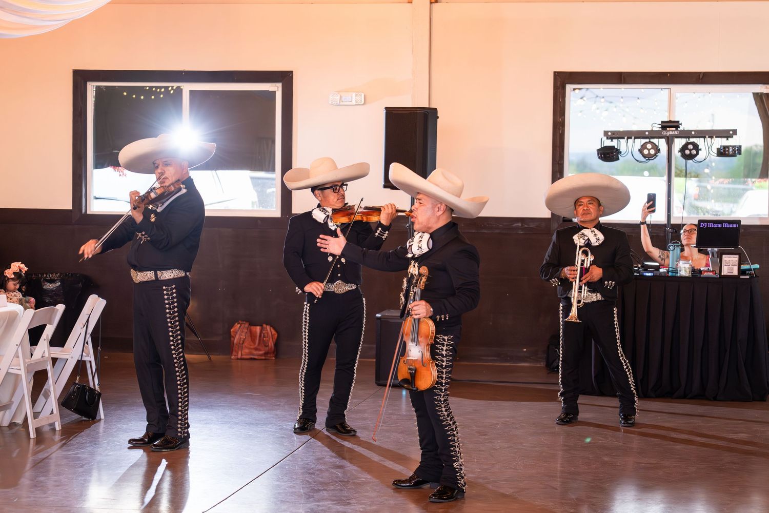Mariachi band in traditional charro suits and sombreros performing with violins at an indoor event venue.