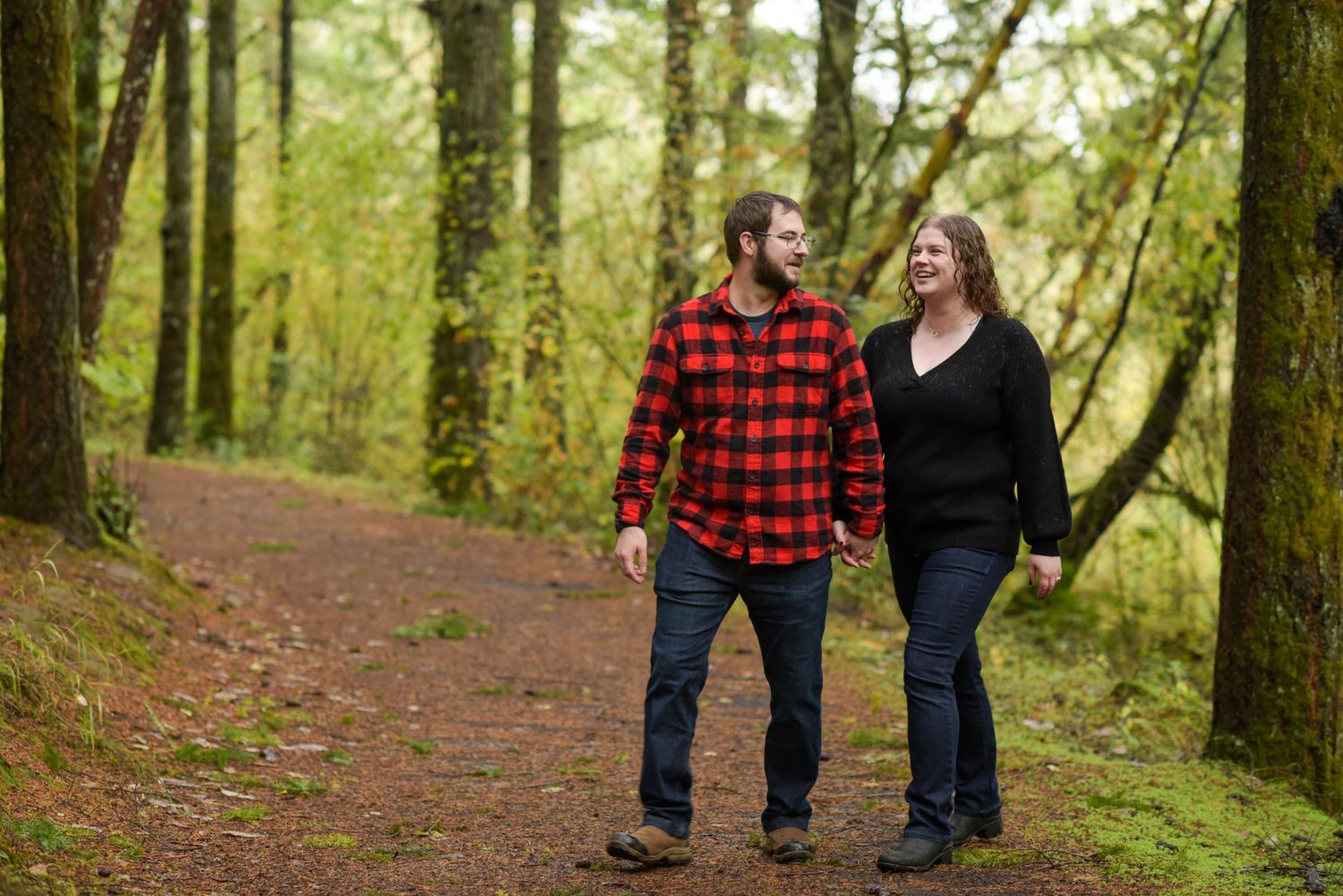 Couple strolling together on a wooded trail surrounded by evergreen trees.