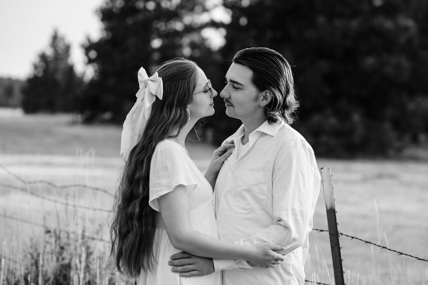 A romantic black and white portrait of a couple sharing an intimate moment in a rustic outdoor setting.