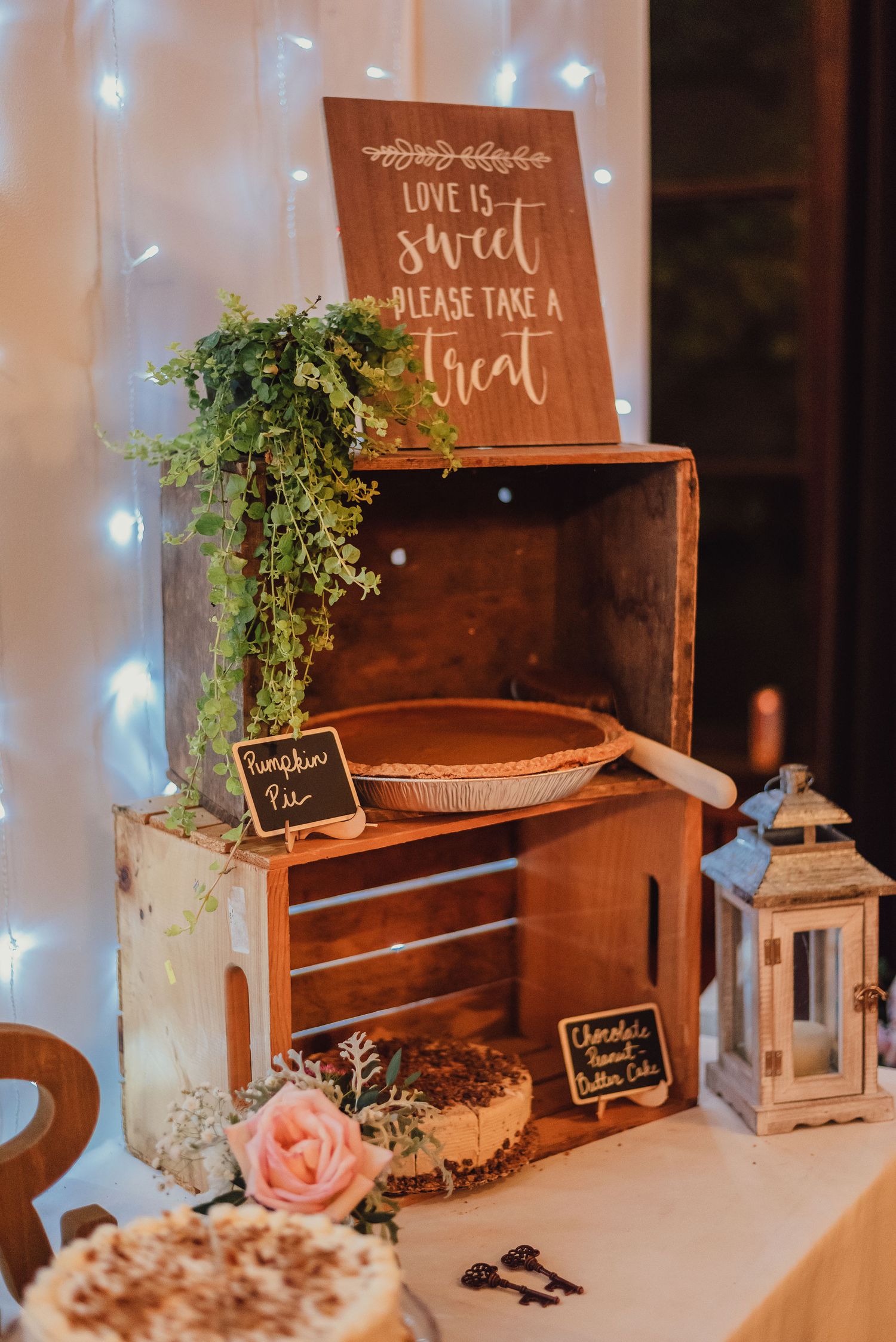 A rustic wooden crate wedding dessert display with 'Love is Sweet' signage and lantern decor.