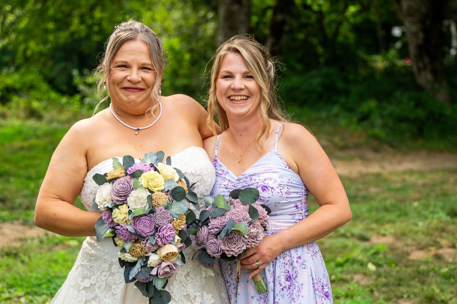 Wedding party members in lavender dresses hold colorful bouquets while posing outdoors.