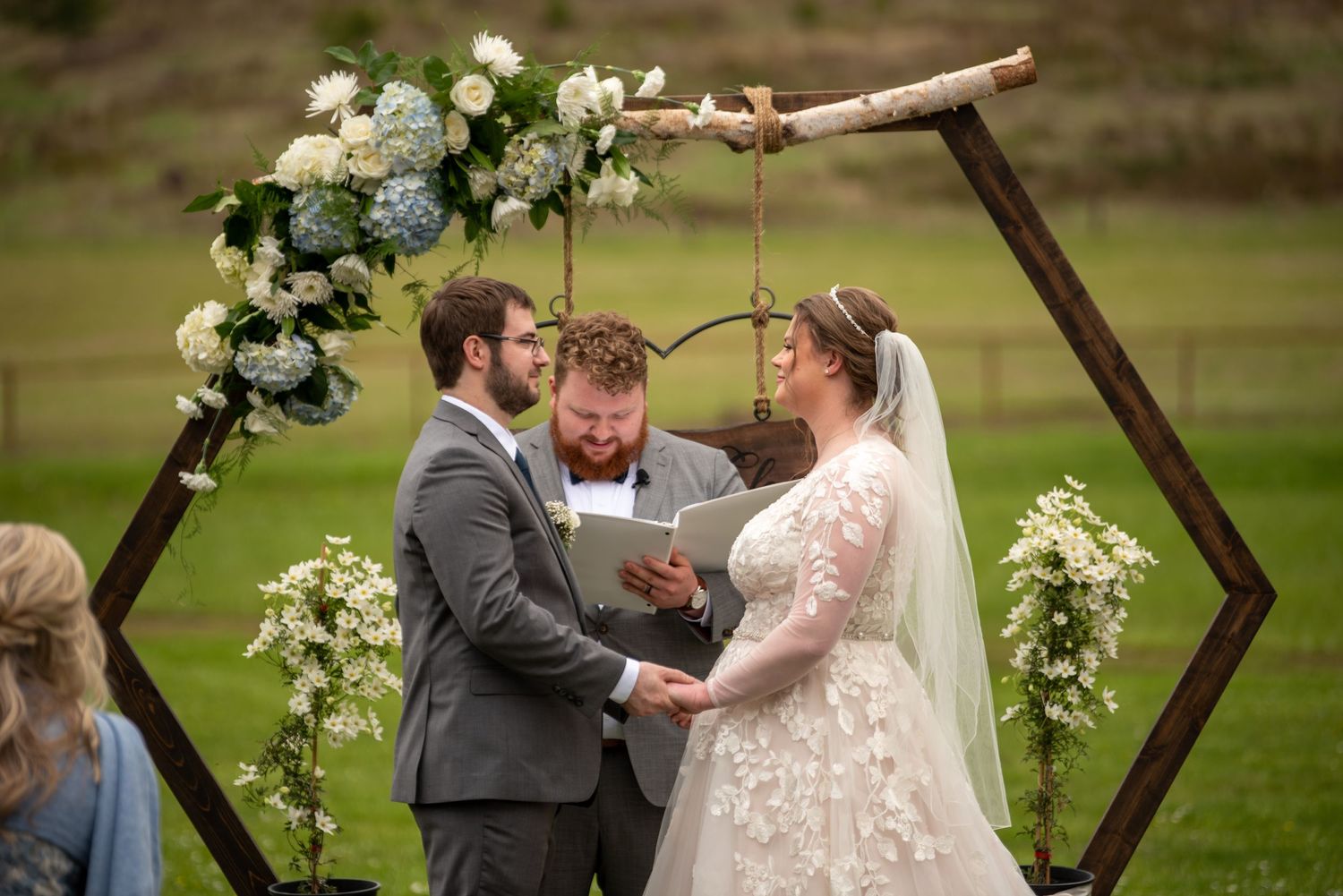 Wedding ceremony under wooden hexagonal arch decorated with white roses and greenery.