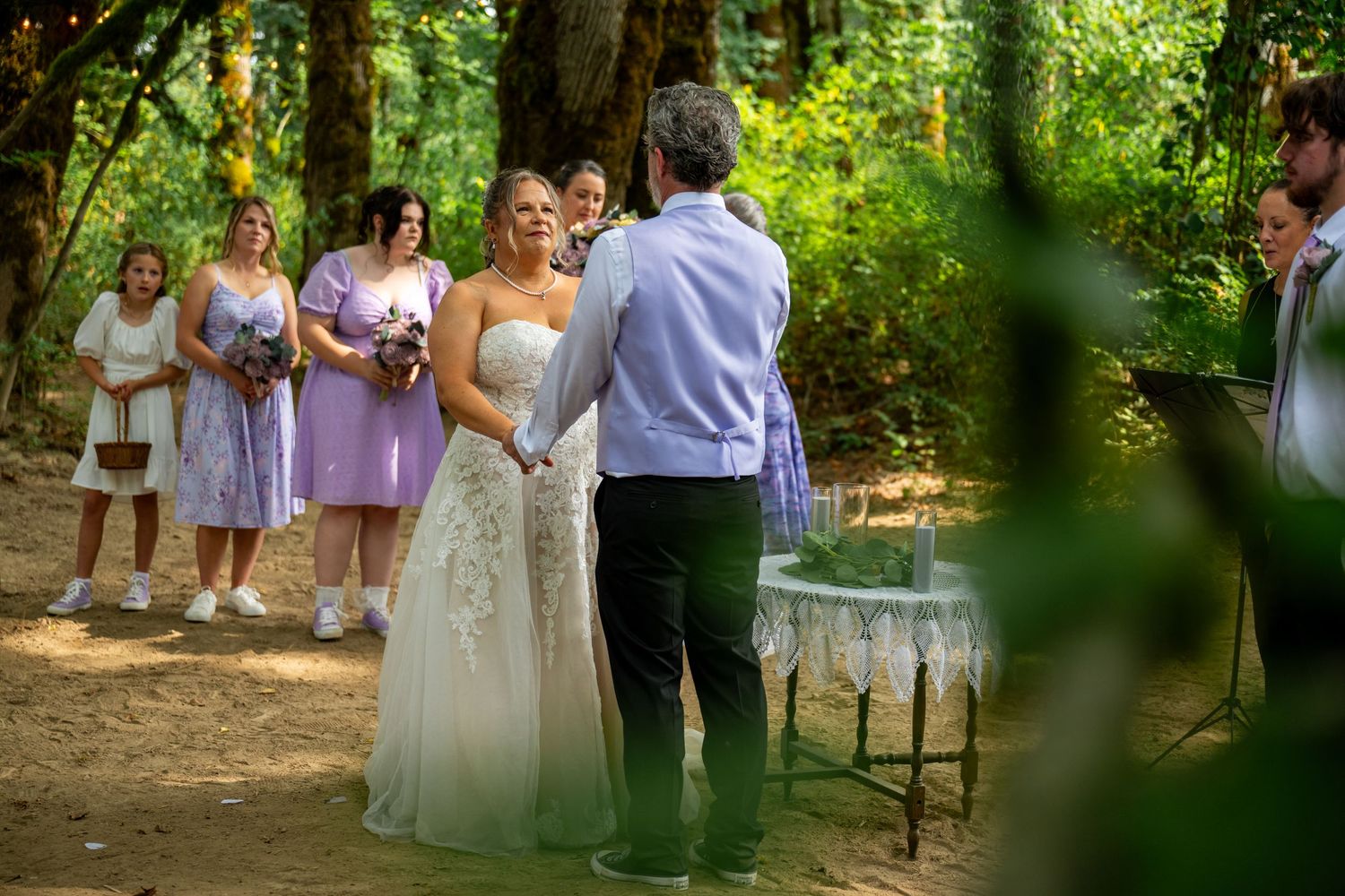 Outdoor forest wedding ceremony with bridesmaids in purple dresses.