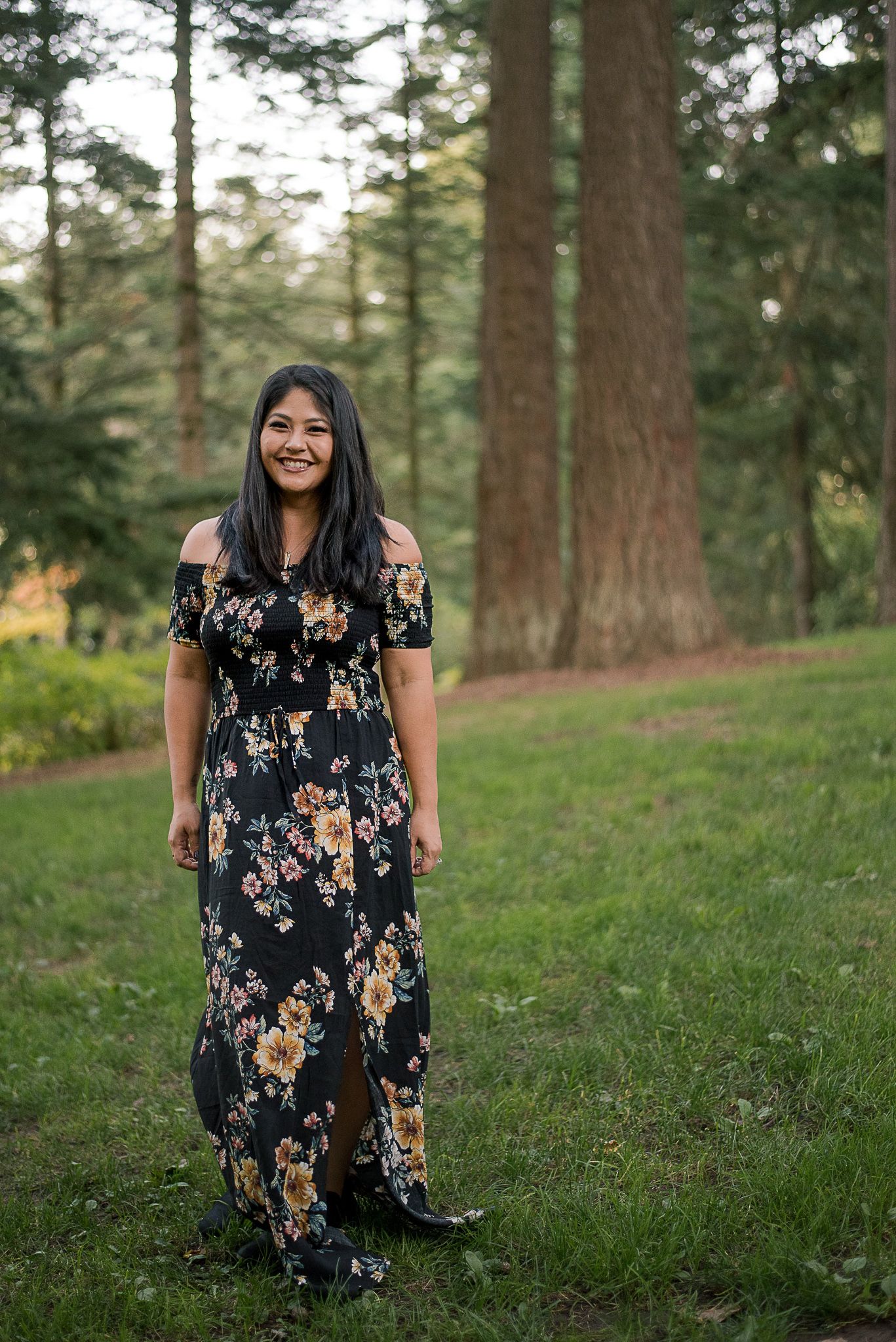 A woman in a floral dress poses in a serene forest setting.