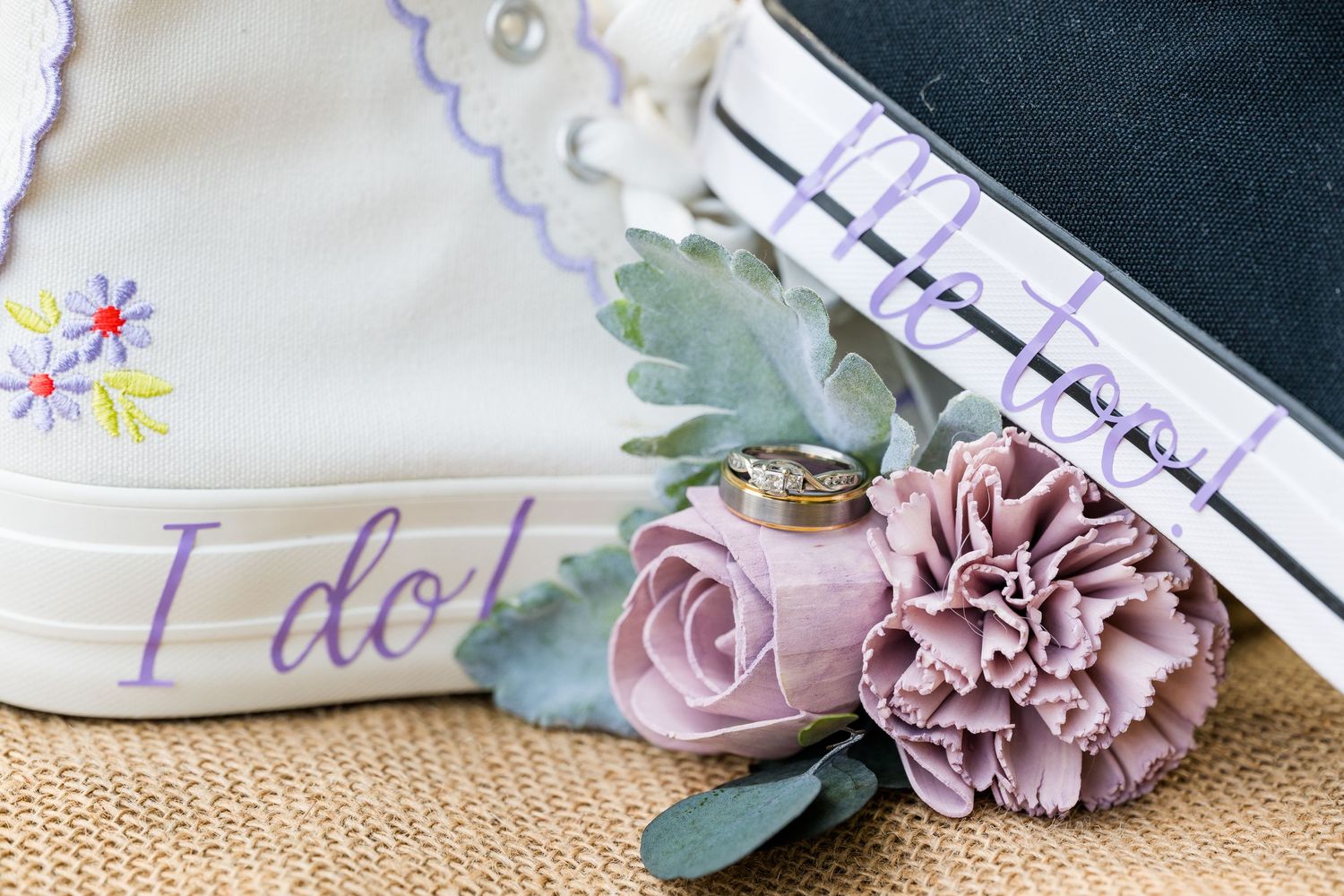 Wedding details flat lay featuring converse shoes, rings, and floral boutonniere on burlap.