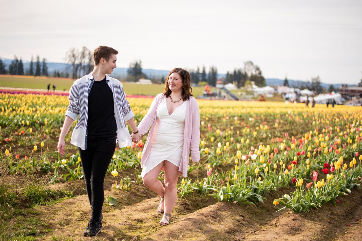 A couple walks hand in hand through colorful tulip fields on a cloudy day.