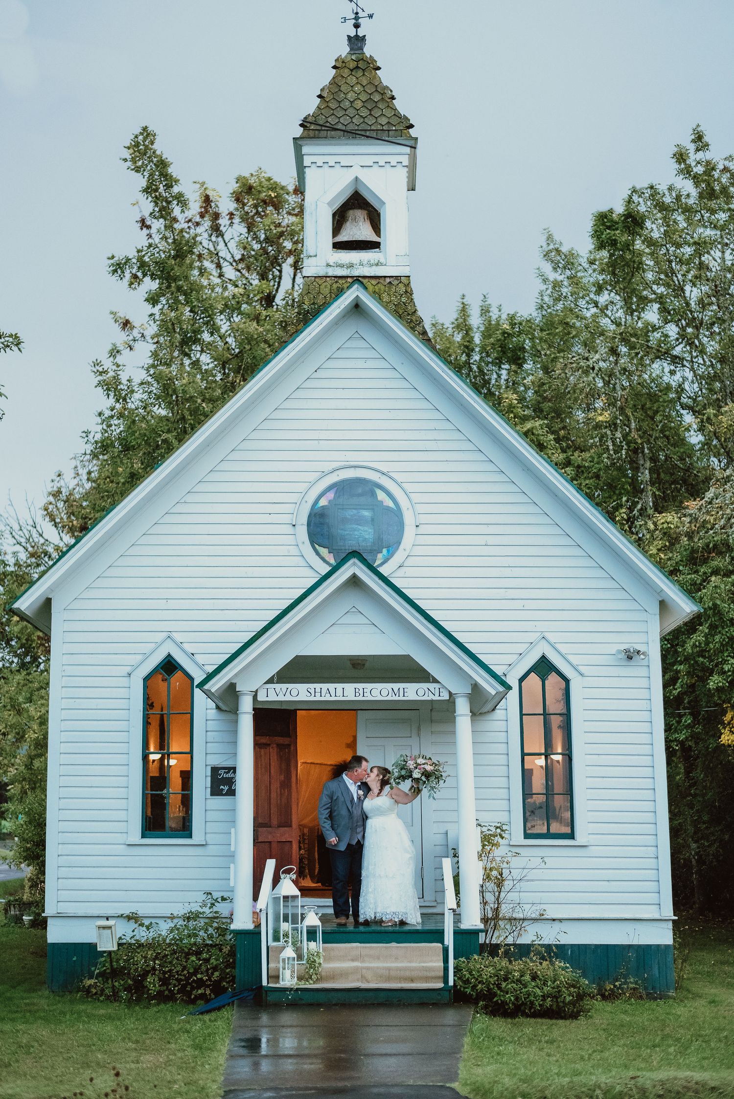 A charming white chapel with a bell tower and round window on a rainy wedding day.
