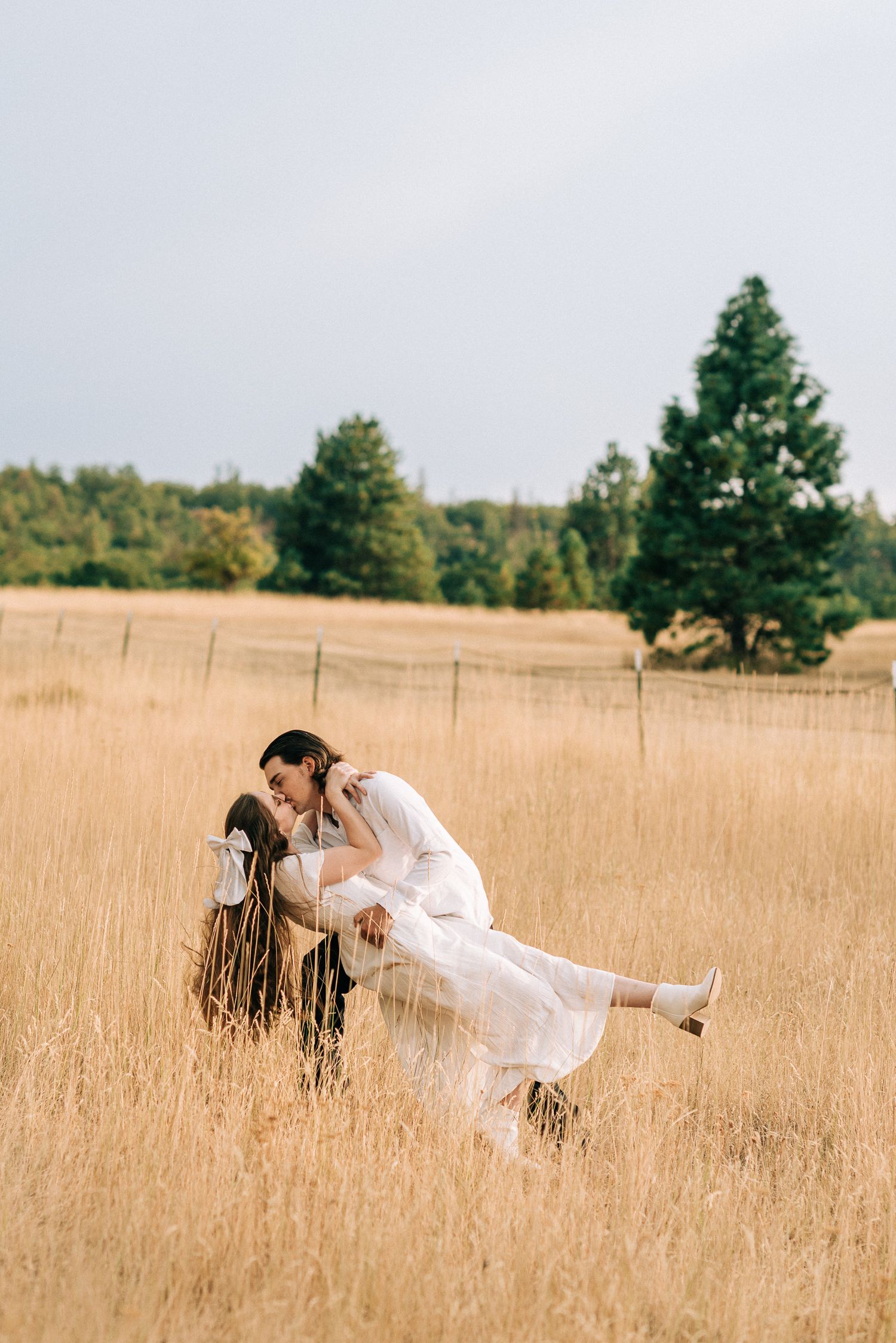 Groom dipping bride in a golden wheat field with trees in the background.