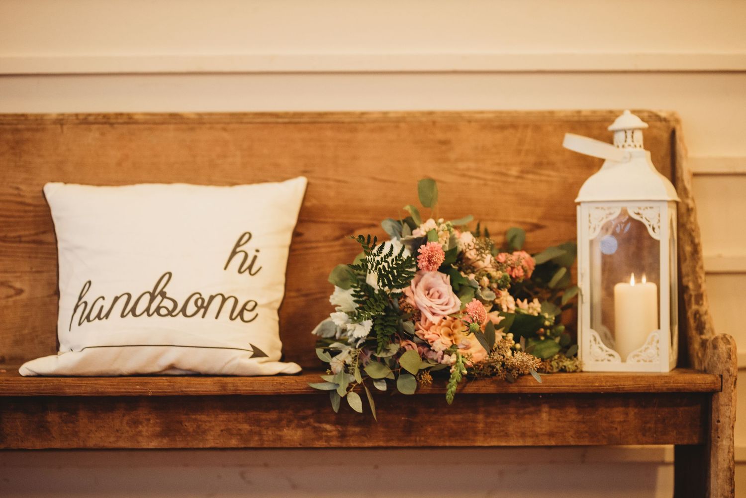 Rustic wedding decor with wooden shelf displaying 'hi' and 'handsome' pillows with floral arrangements.