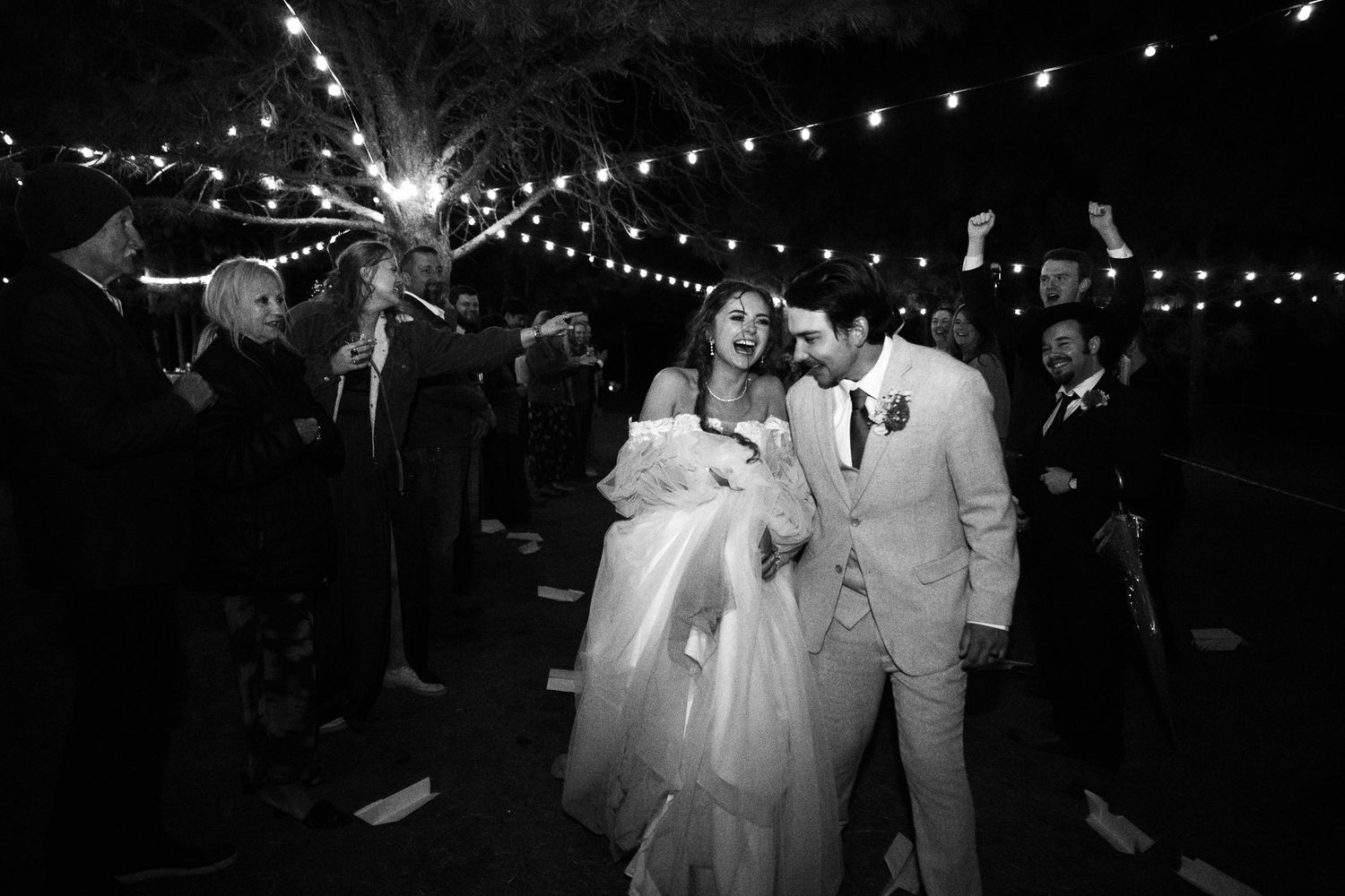 A couple walks under string lights at their nighttime wedding reception while guests hold sparklers.