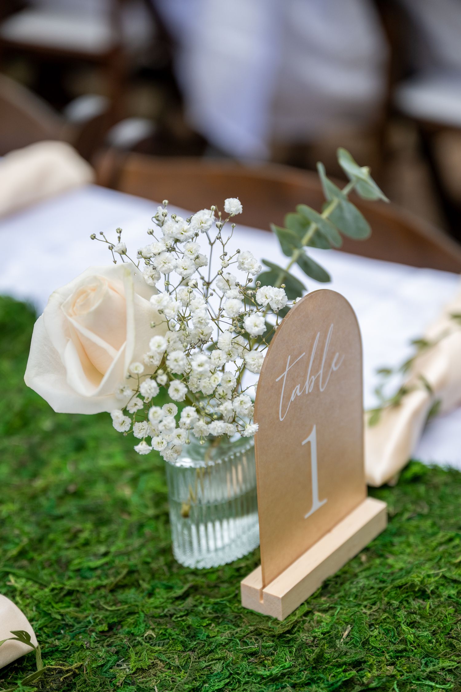 A white rose, baby's breathe and eucalyptus set in a glass vase in front of a table number at an oregon wedding