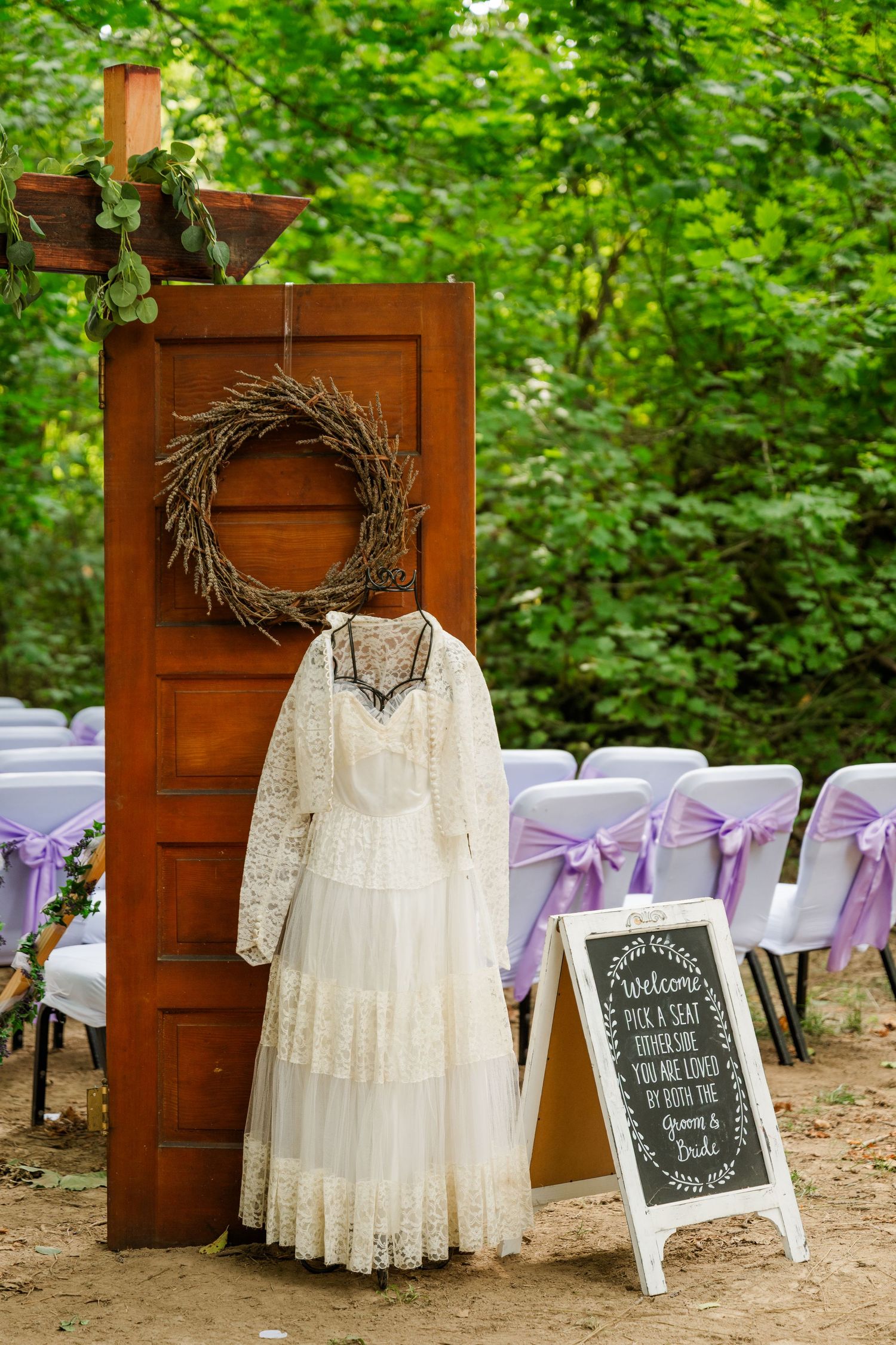 Vintage wedding dress display with purple chair decorations and chalkboard signs at outdoor venue.