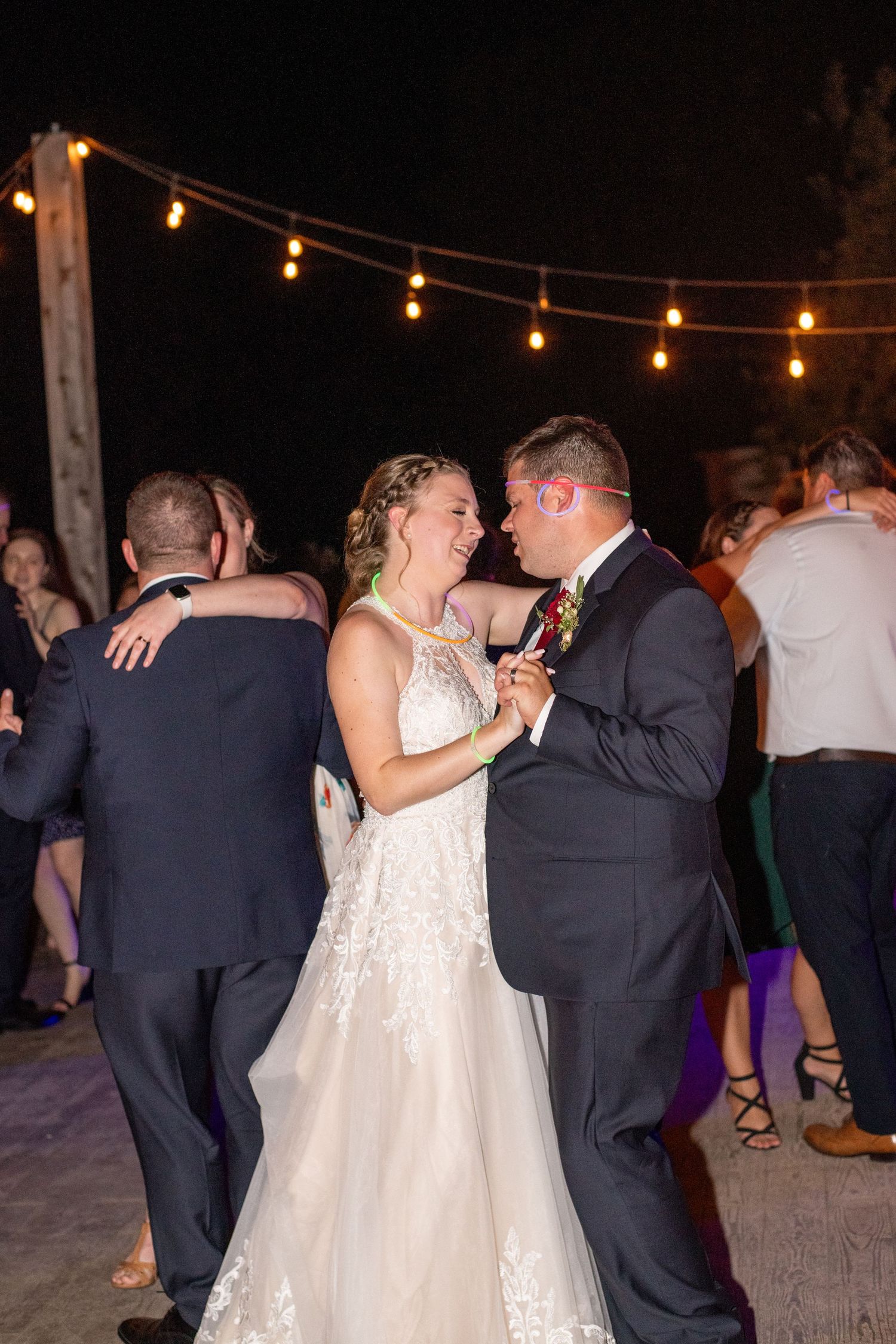 Couples dancing together at an outdoor evening reception under warm string lights.