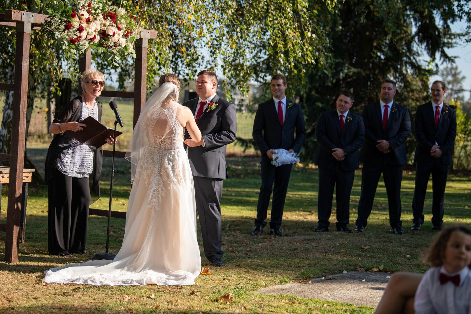 Outdoor wedding ceremony setup with wooden cross and guests gathered under trees.