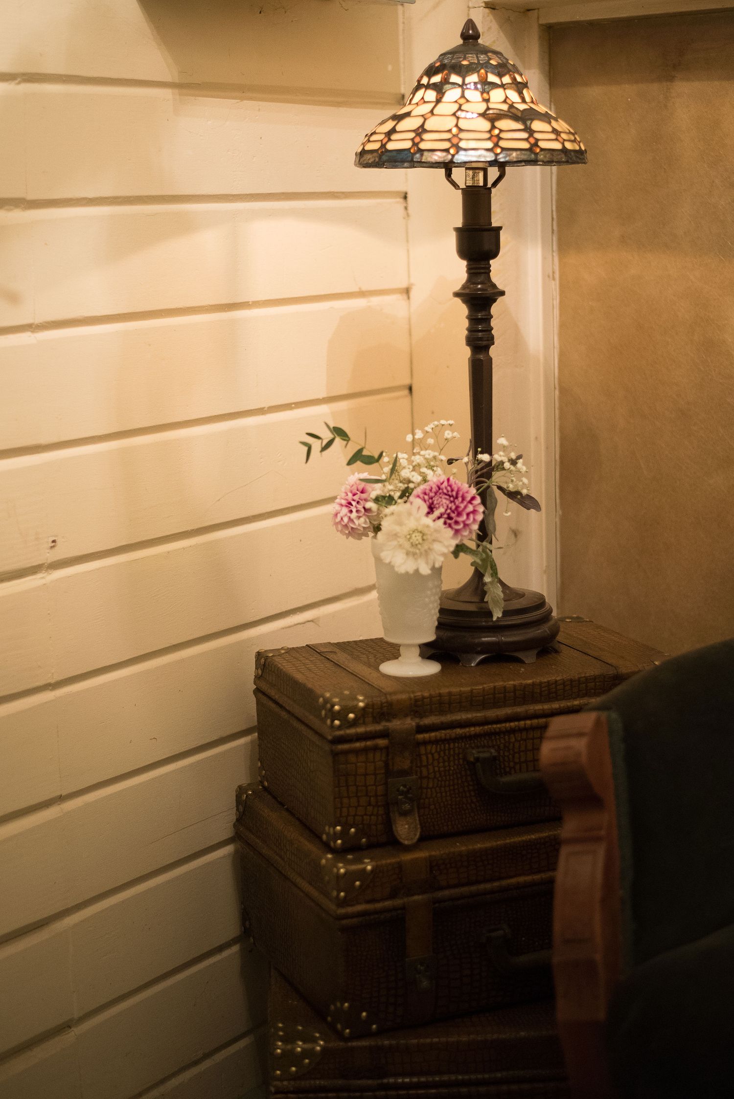 A vintage Tiffany-style lamp and pink flowers on an antique side table.
