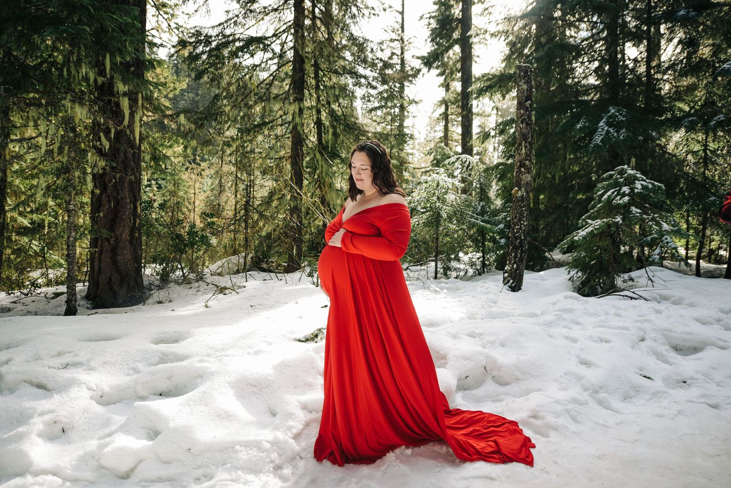 A red dress billows gracefully against pristine snow in a winter forest setting.