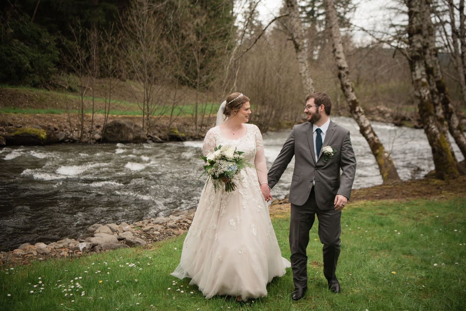 A newlywed couple poses by a rushing stream surrounded by lush greenery.