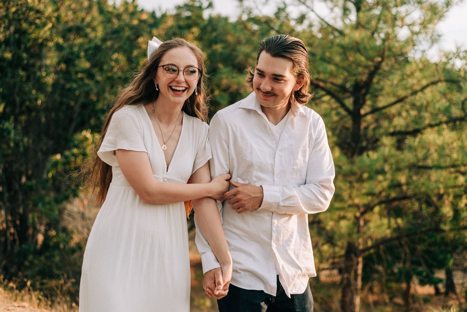 A laughing couple in white clothing sharing a playful moment outdoors.