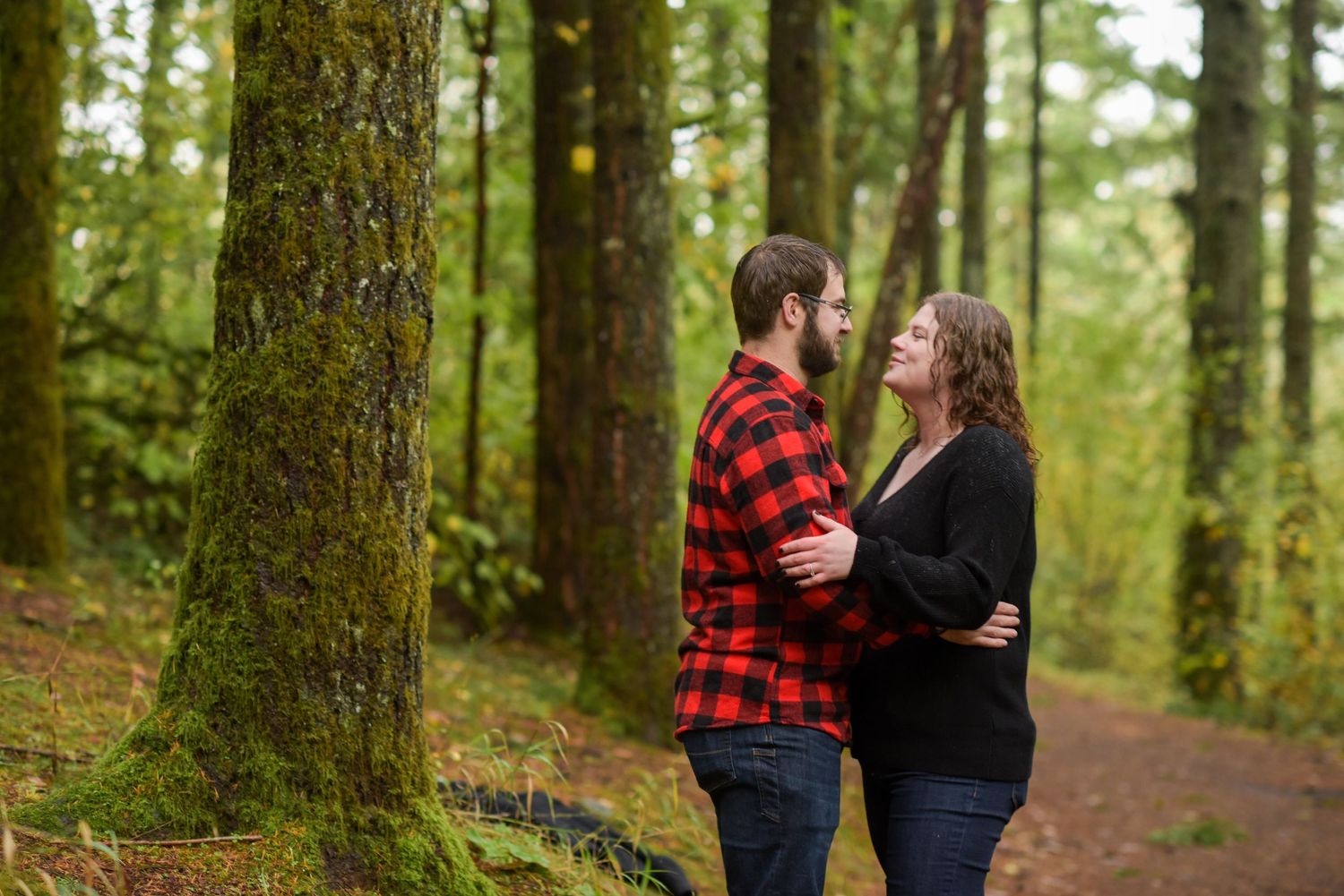 Couple walking hand in hand through a lush green forest path.