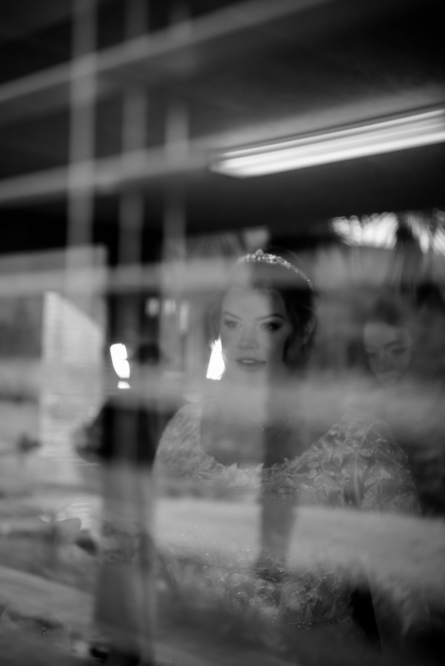 Artistic black and white reflection portrait of a bride in her wedding gown captured through a glass window.