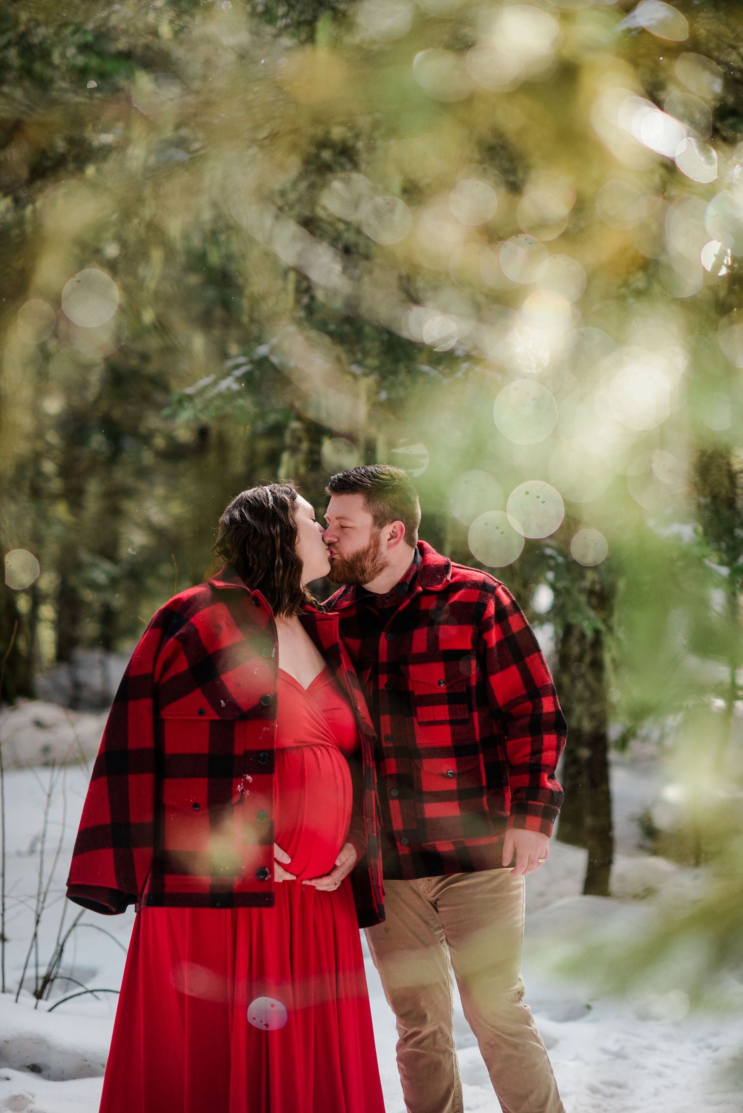 Romantic winter portrait through bokeh branches in snowy forest setting.