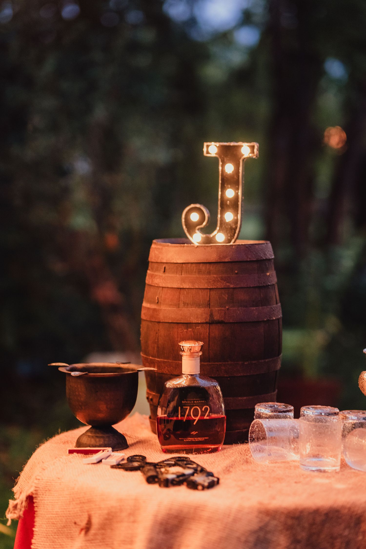 A rustic wedding display with an illuminated letter J, barrel, and vintage decor.